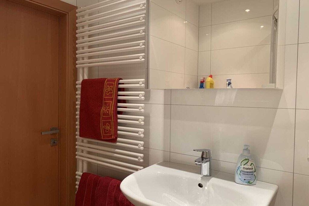 Une salle de bain avec un lavabo blanc, un miroir, un porte-serviettes avec une serviette rouge et des articles de toilette posés sur le comptoir.