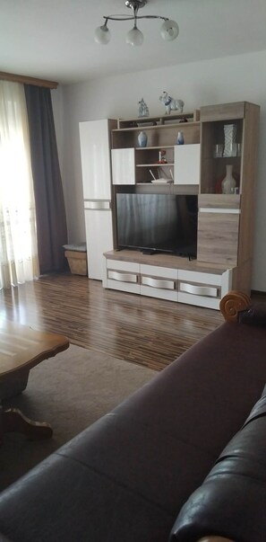 Un soggiorno con TV a schermo piatto, pavimento in legno, un divano e una lampada a sospensione.