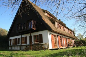 A traditional thatched-roof house with a balcony, wooden shutters, and a stone wall foundation. - - The Fox Den Apartment II (Meesiger)