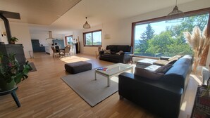Ein modernes Wohnzimmer mit Essbereich, einer Couch, einem Couchtisch und Blick ins Freie.