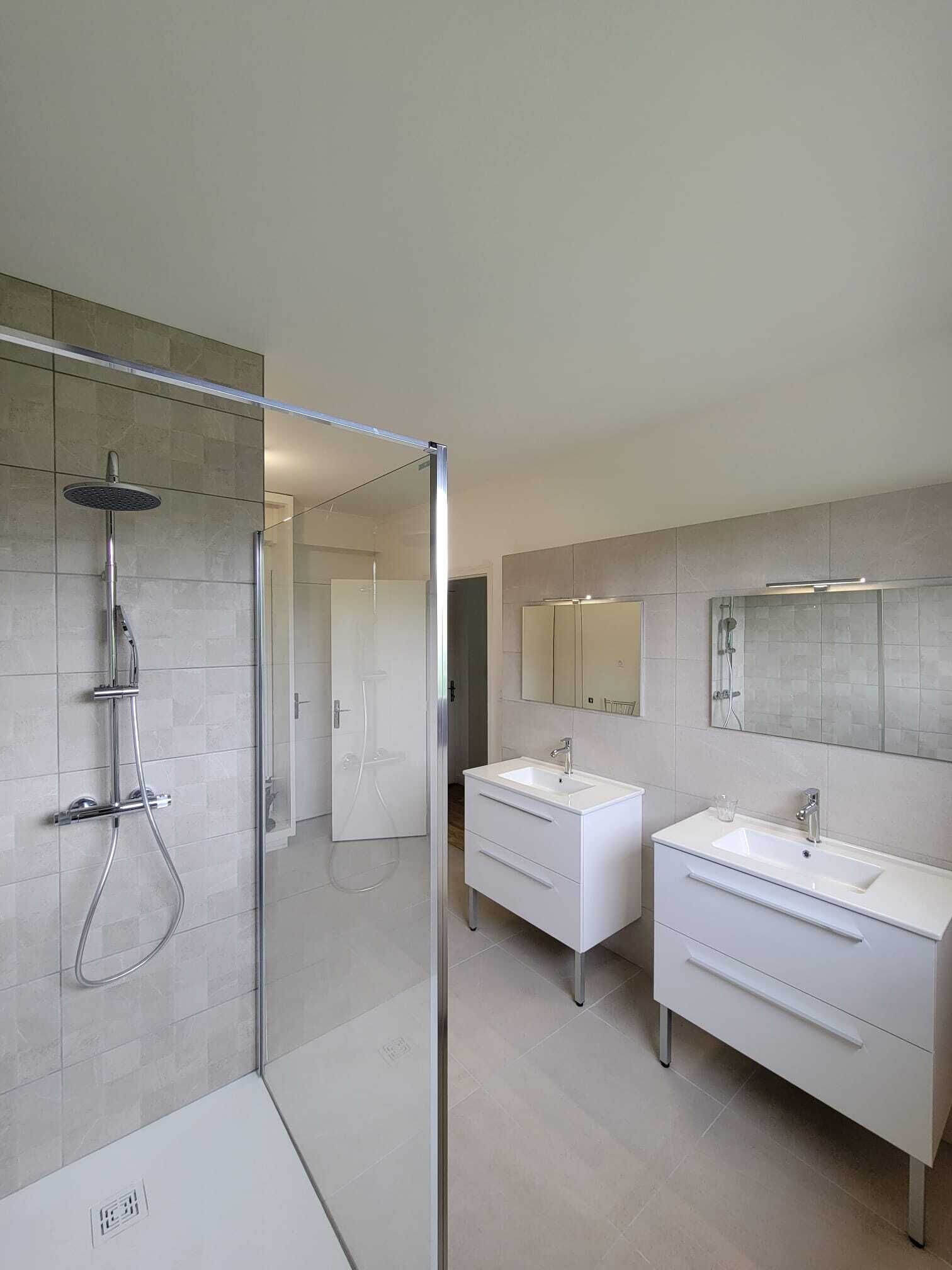 A modern bathroom with a glass-enclosed shower, two white vanity units, and a large mirror.