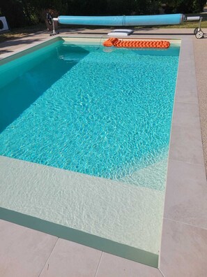 Ein rechteckiger Swimmingpool mit klarem, blauem Wasser, umgeben von einer gefliesten Liegefläche.