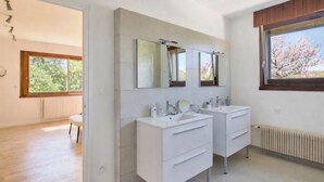 Ein modernes Badezimmer mit zwei Waschbecken, einem großen Spiegel und einem Fenster mit Blick auf Bäume.