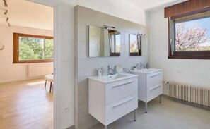 Une salle de bain moderne avec deux lavabos, un grand miroir et une fenêtre donnant sur la verdure.