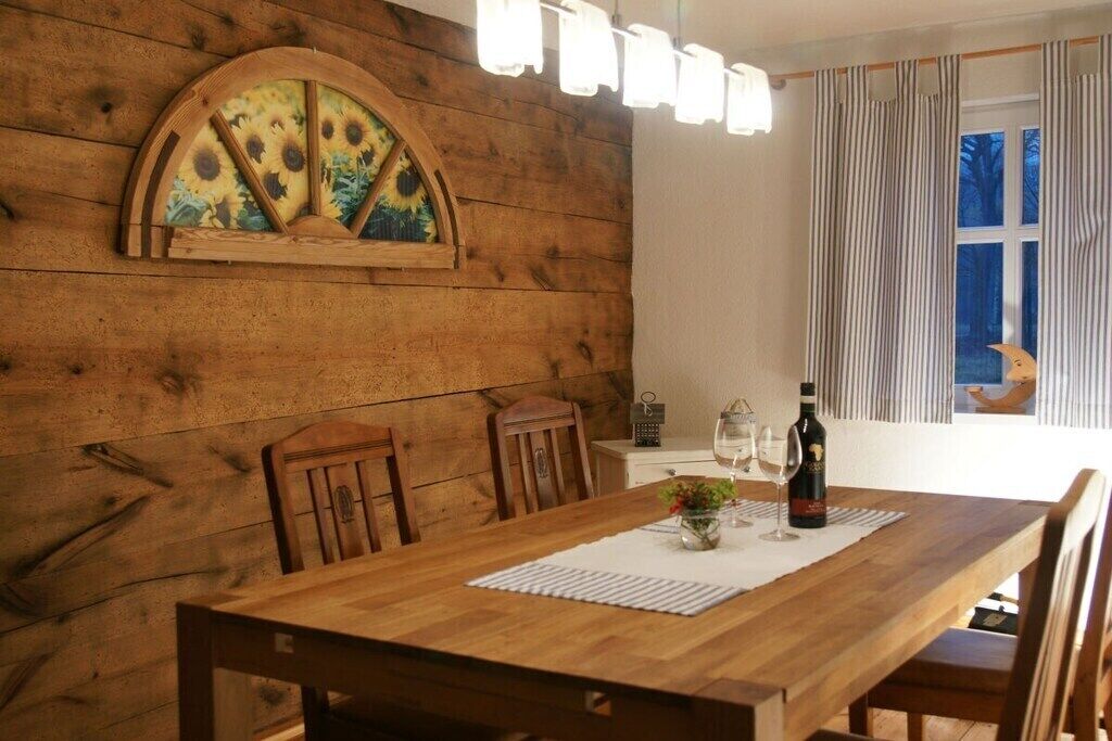 A wooden dining table with chairs, a wine bottle, and a vase with flowers.