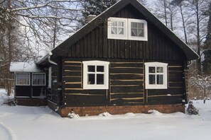 Eine Blockhütte mit zwei Fenstern und einem Schornstein, umgeben von Schnee.