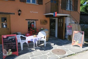 An outdoor seating area with a stone floor, white plastic chairs, a table with a tablecloth, and a menu stand. - Holiday home in Magadino with swimming pool (Magadino)