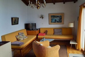 A living room with a sofa, armchair, television, and artwork on the wall. - Holiday home in Magadino with swimming pool (Magadino)
