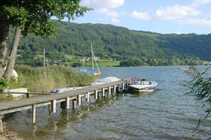 Ein ruhiger See mit Booten, die an einem hölzernen Steg vertäut sind, umgeben von üppiger Vegetation und Hügeln.