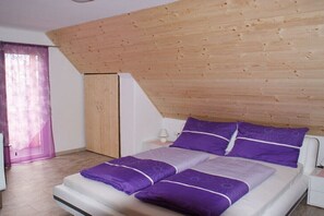 A bedroom with a sloped ceiling, a bed with purple bedding, a wooden wardrobe, and a nightstand with a lamp. - "large holiday home" (Bodensdorf am Ossiachersee)