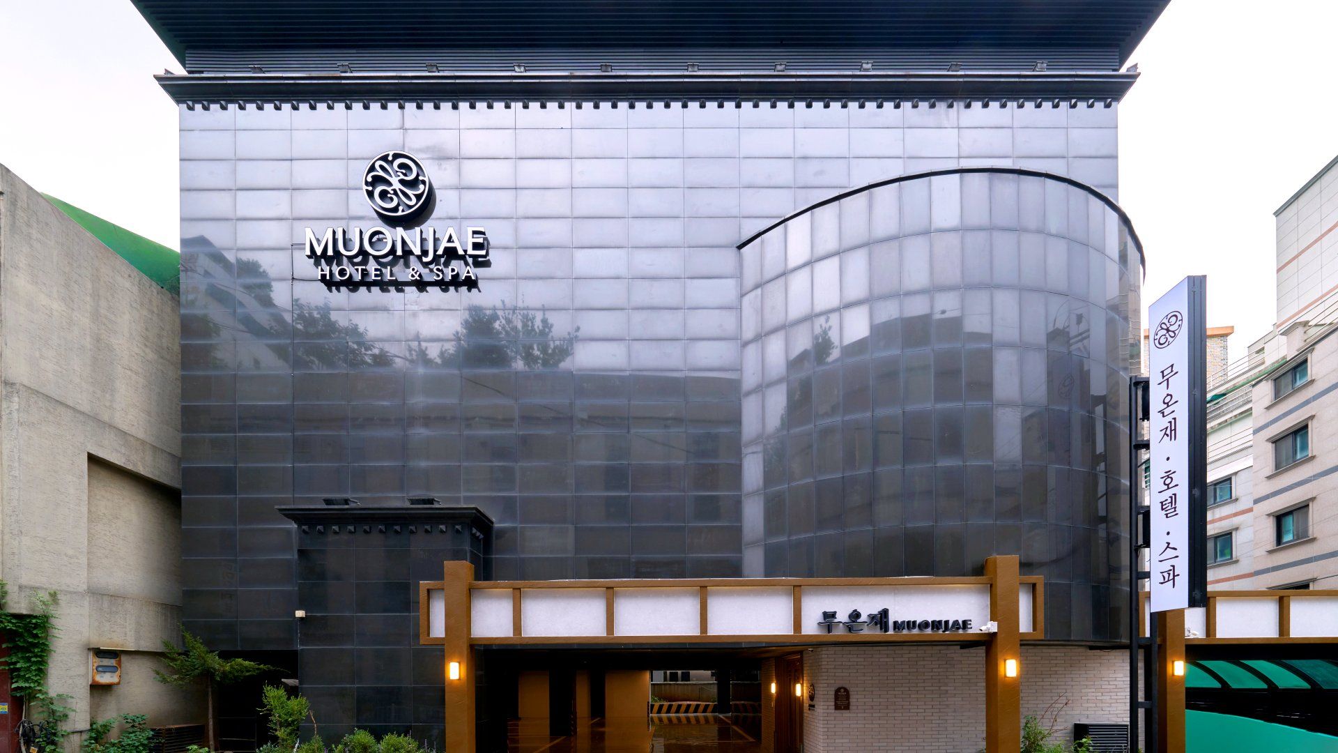 En hotellfasad med ett stort glasfönster och en skylt med texten ”MUONJAE HOTEL & SPA”.