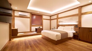 Un dormitorio moderno con suelo de madera, una cama con ropa de cama blanca, una mesita de noche y un aire acondicionado instalado en la pared, además de una ventana con persianas.