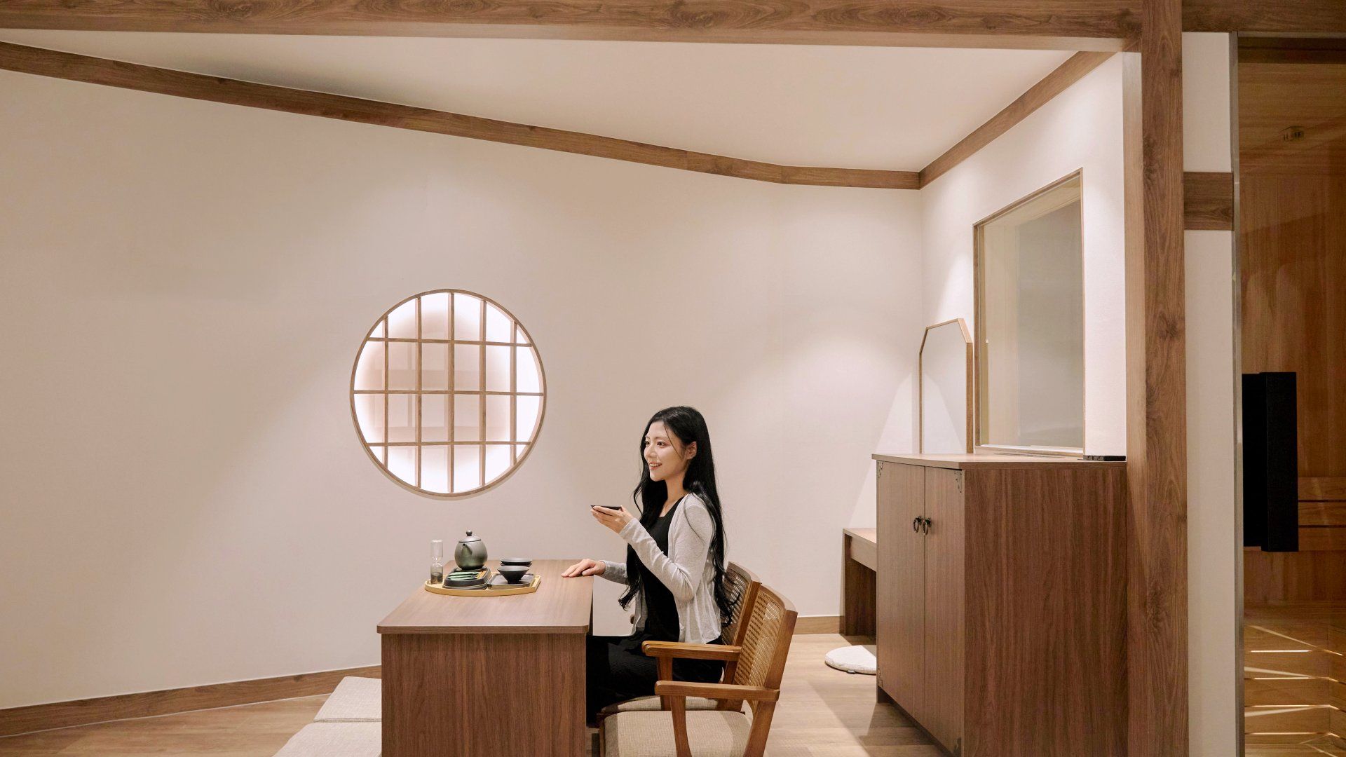 A room with a round window, a wooden cabinet, and a table with a tea set.