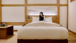 A neatly made bed with a wooden headboard, a bedside table with a teapot, and a wall with a wooden panel design. - Muonjae by Anook Suwon Heanggung (Suwon)