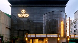 Un hotel moderno con una amplia fachada de vidrio, un letrero llamativo para MuonJae Hotel & Spa y una entrada bien iluminada.