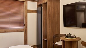 Una habitación con cama, un armario de madera, televisor y una pequeña mesa con tetera y vaso.