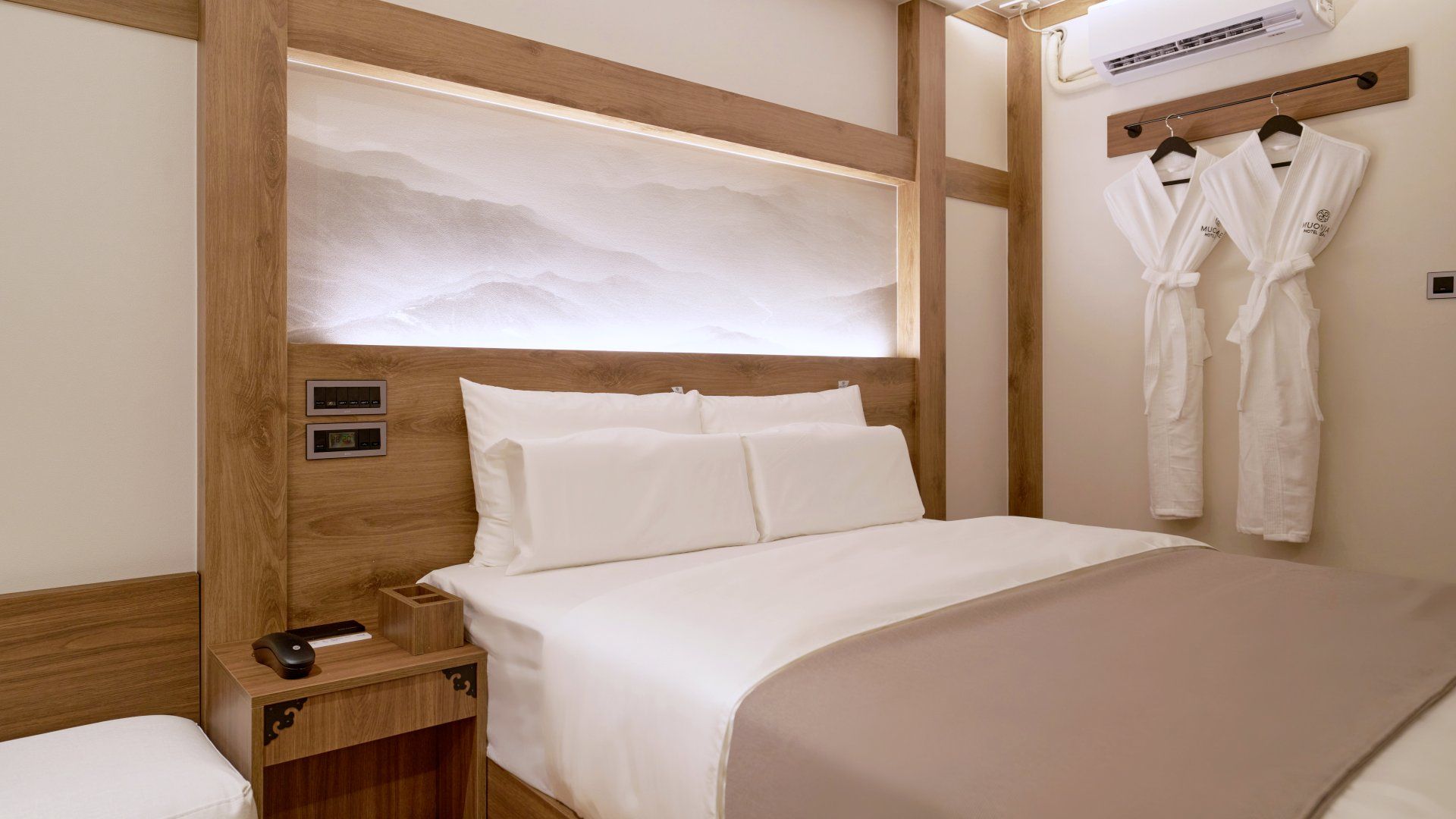 A hotel room with a bed, bedside controls, a nightstand, a robe rack, and an air conditioning unit.