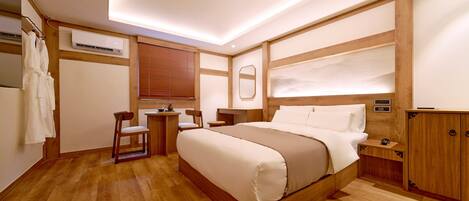 Ein Hotelzimmer mit einem großen Bett, Holzmöbeln, einem kleinen Tisch, Stühlen, einer Klimaanlage und einem Kleiderschrank.