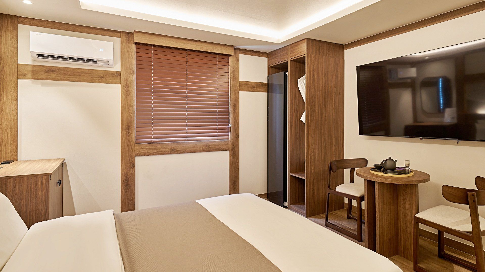 A hotel room with a bed, a desk, a TV, and a window with blinds.