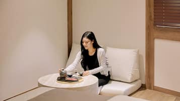 Une personne assise sur un canapé, devant une table, tenant une théière.