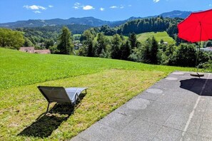 A paved pathway with a red umbrella and a chair on grass, overlooking a green field and distant hills. - South-facing slope of Rüschegg (Rüschegg-Heubach)