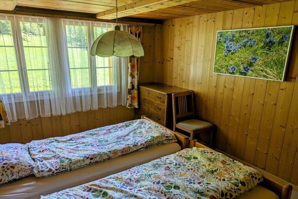 Una habitació amb dos llits, un escriptori de fusta, una cadira i una finestra amb cortines.