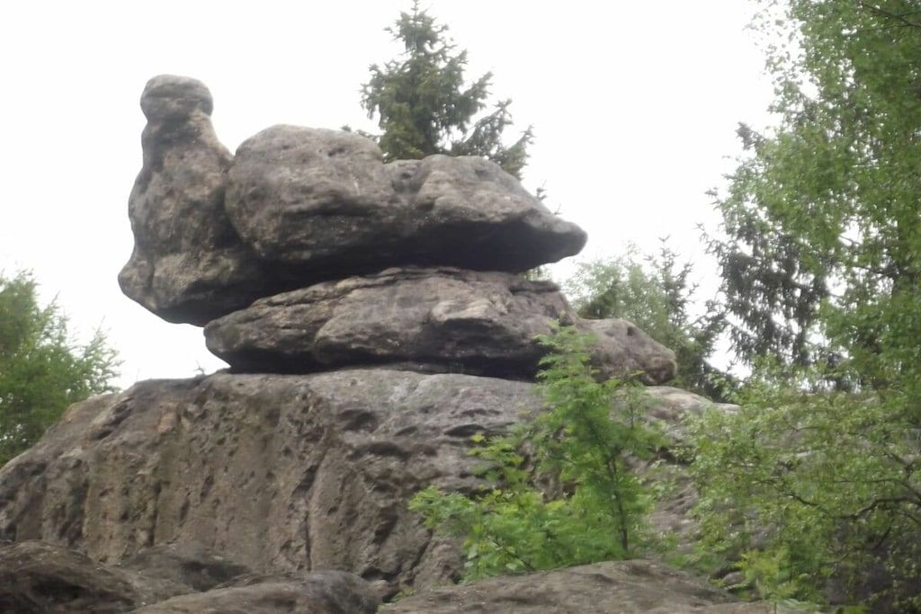 A large rock formation with a balanced rock on top, surrounded by greenery.