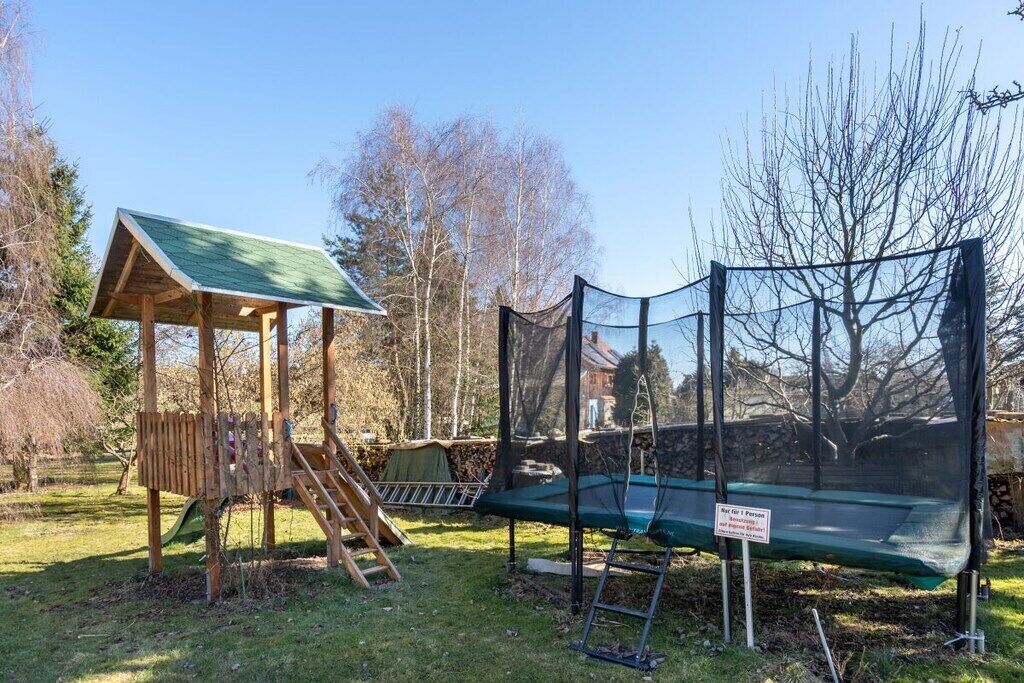 Un parque infantil con columpios y un trampolín, todo rodeado por una red de seguridad.