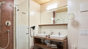 Un baño moderno con cabina de ducha de vidrio, dos lavabos, un tocador con espejo y un inodoro.