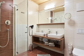 A modern bathroom with a glass shower enclosure, two sinks, a vanity with a mirror, and a toilet. - Vrbo Property (Lermoos)