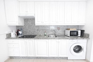 Una cocina con armarios blancos, encimera de granito, microondas, lavaplatos y lavadora.