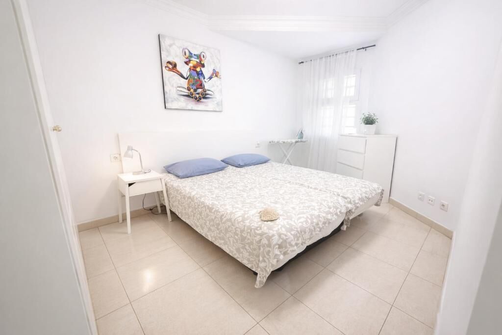 Un dormitorio con cama, escritorio, silla, ventana con cortinas y una obra de arte en la pared.