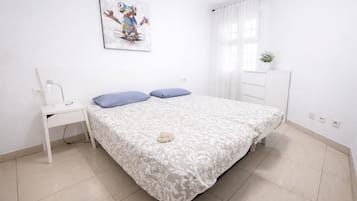 Un dormitorio con cama, mesita de noche, lámpara de pared, ventana con cortinas y una planta pequeña en maceta.