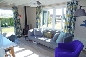 A room with a sofa, a purple chair, a dining table, and a view through large windows. - Holiday home with 2 bedrooms (Westende-Dorp)
