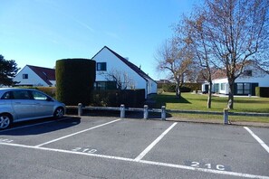 A parking lot with marked spaces, a white building, and a tree. - Holiday home with 2 bedrooms (Westende-Dorp)