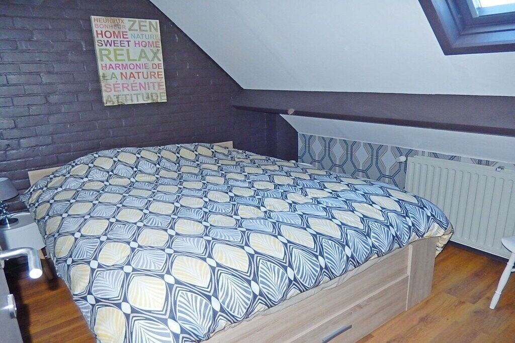 A bedroom with a patterned bedspread, a skylight, a radiator, and a wall with multilingual motivational phrases.