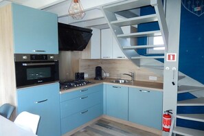 A compact kitchen with a stove, oven, and sink, a blue chair, and a white staircase. - Holiday home with 2 bedrooms (Westende-Dorp)