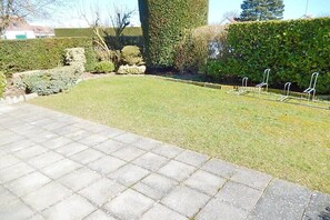 A paved area with a grassy lawn, a hedge, and metal chairs. - Holiday home with 2 bedrooms (Westende-Dorp)