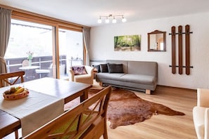 Ein Wohnzimmer mit einer Couch, einem Esstisch mit Stühlen, einem Kuhfellteppich und einem großen Fenster mit Vorhängen.