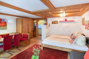Un salon chaleureux avec un canapé, des fauteuils rouges, des poutres en bois et un tapis rouge.