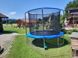 A trampoline with a safety net, surrounded by a grassy area and a wooden fence. - Wirtsstubn Vacation Rental, 75 m², Rooftop Terrace, Pool & Hot Tub (Siegsdorf)