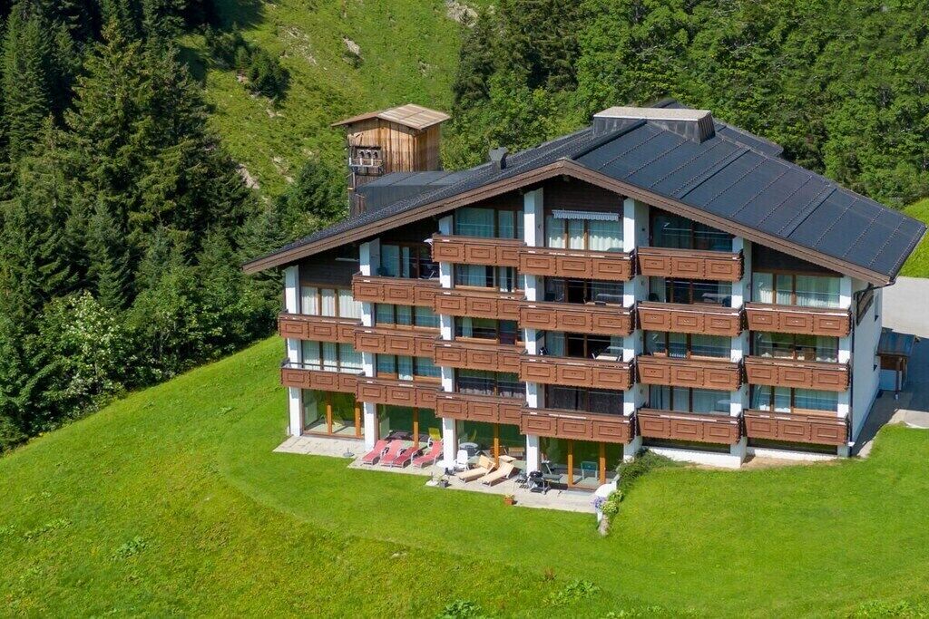 A multi-story hotel with balconies, a ski lift, and a mountainous backdrop.