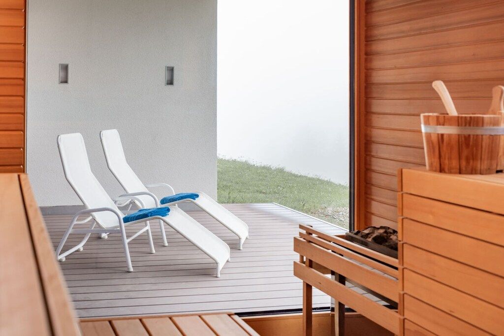 A wooden deck with lounge chairs and a wooden table, overlooking a grassy area.