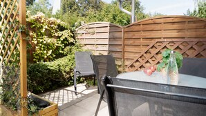En udendørs patio med et bord og stole, omgivet af et træhegn og grøn vegetation.