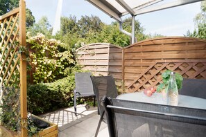 An outdoor patio with a table and chairs, surrounded by a wooden fence and greenery. - Vrbo Property (Kellenhusen)