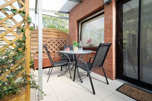 A patio with a round table and four chairs, a wooden fence, and a brick wall. - Vrbo Property (Kellenhusen)