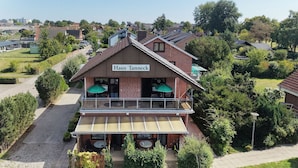En toetagers bygning med et skilt, der viser 'Haus Tanneck'. Den har en balkon med udendørs siddepladser og en overdækket patio.