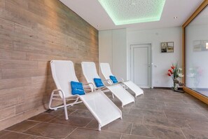 A room with three white sun loungers with blue cushions, a wooden wall, a tiled floor, and a door in the background. - Top 17 for 2-4 people / 2nd floor (Schröcken)