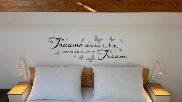A bedroom with a bed, two bedside tables, and a wall with a decorative phrase. - Vacation Rental/Apartment for 6 Guests, 62 m², in Freistadt (317570) (Freistadt)