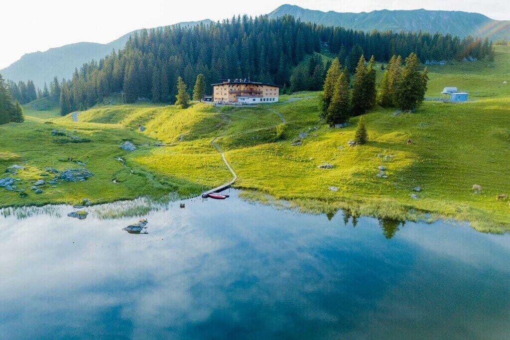 Ein Anwesen am Seeufer mit einem Gebäude, einem Steg und einem bewaldeten Berg im Hintergrund.